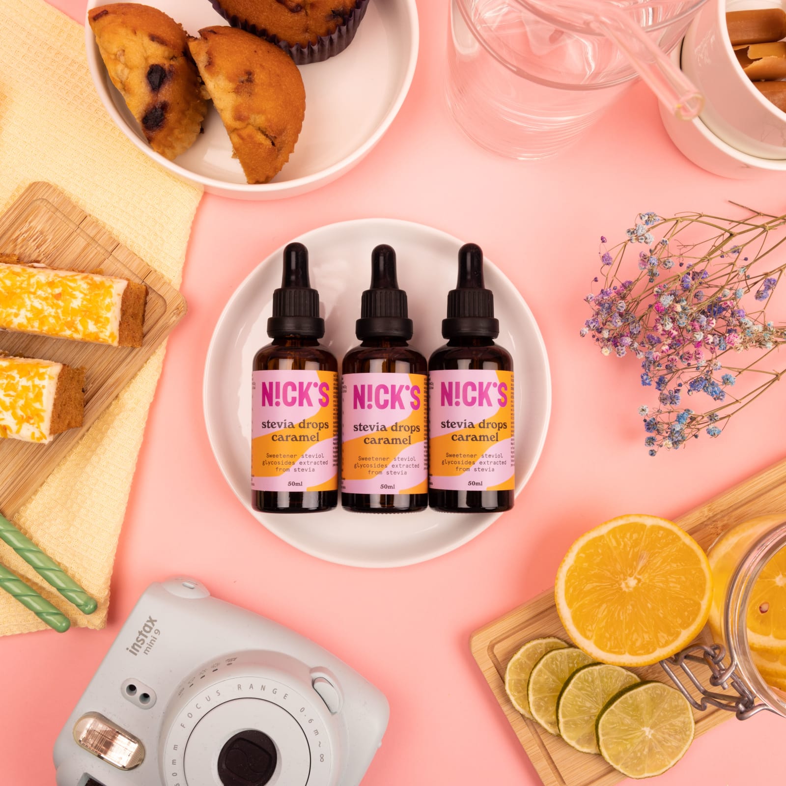 Nick's stevia drops caramel på et lyserosa bord med bakverk og sitrus